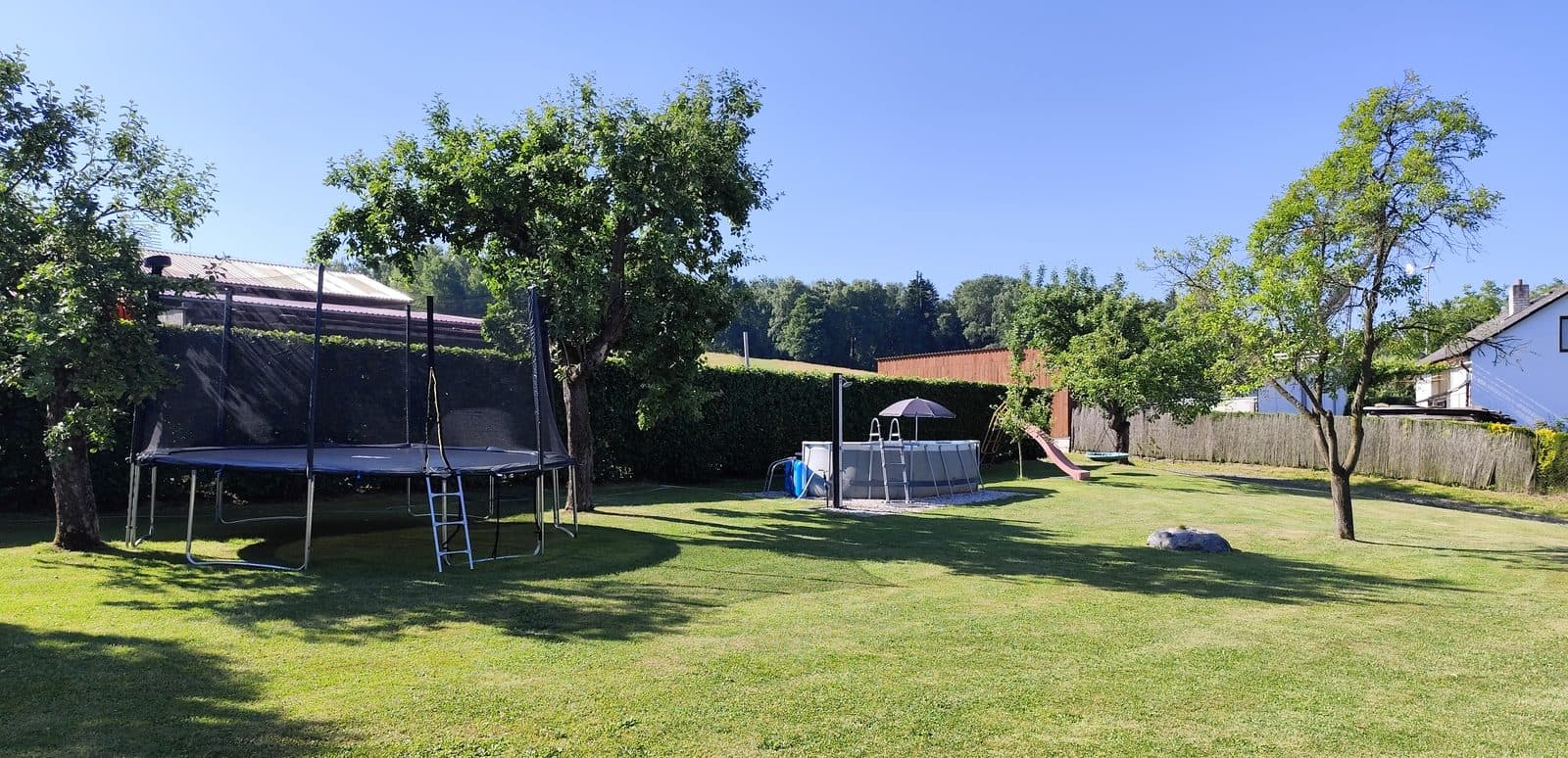 Zahrada se stromy a trampolínou